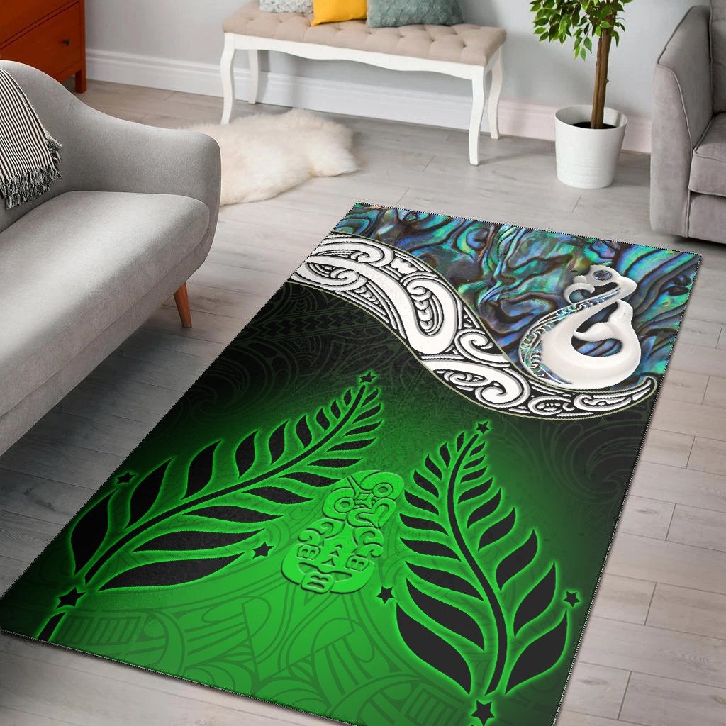 Green area rug with glittery blue shell motif, white Maori-style face, and fern patterns